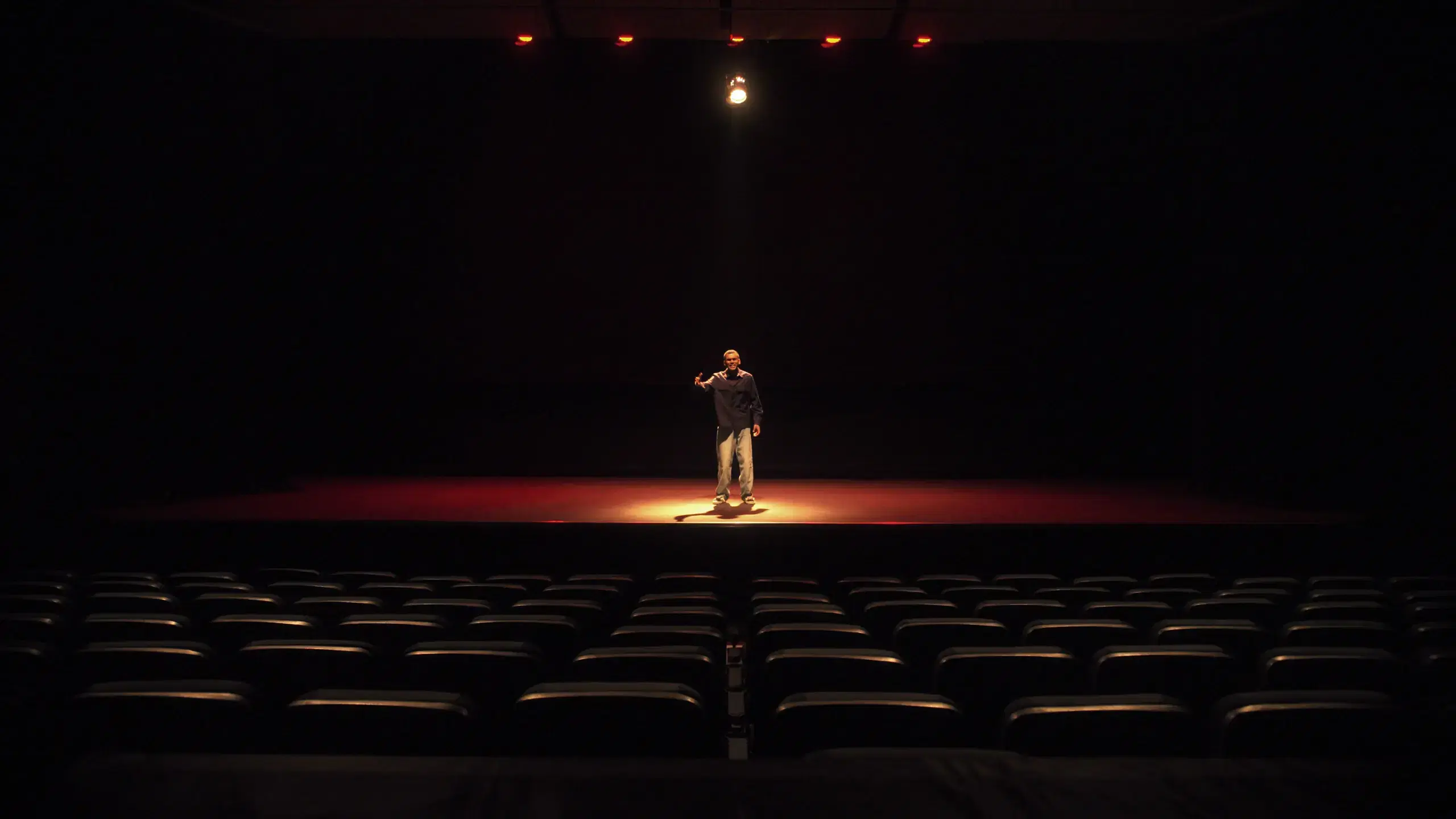 Performer alone on a spotlit stage in front of empty theatre seats