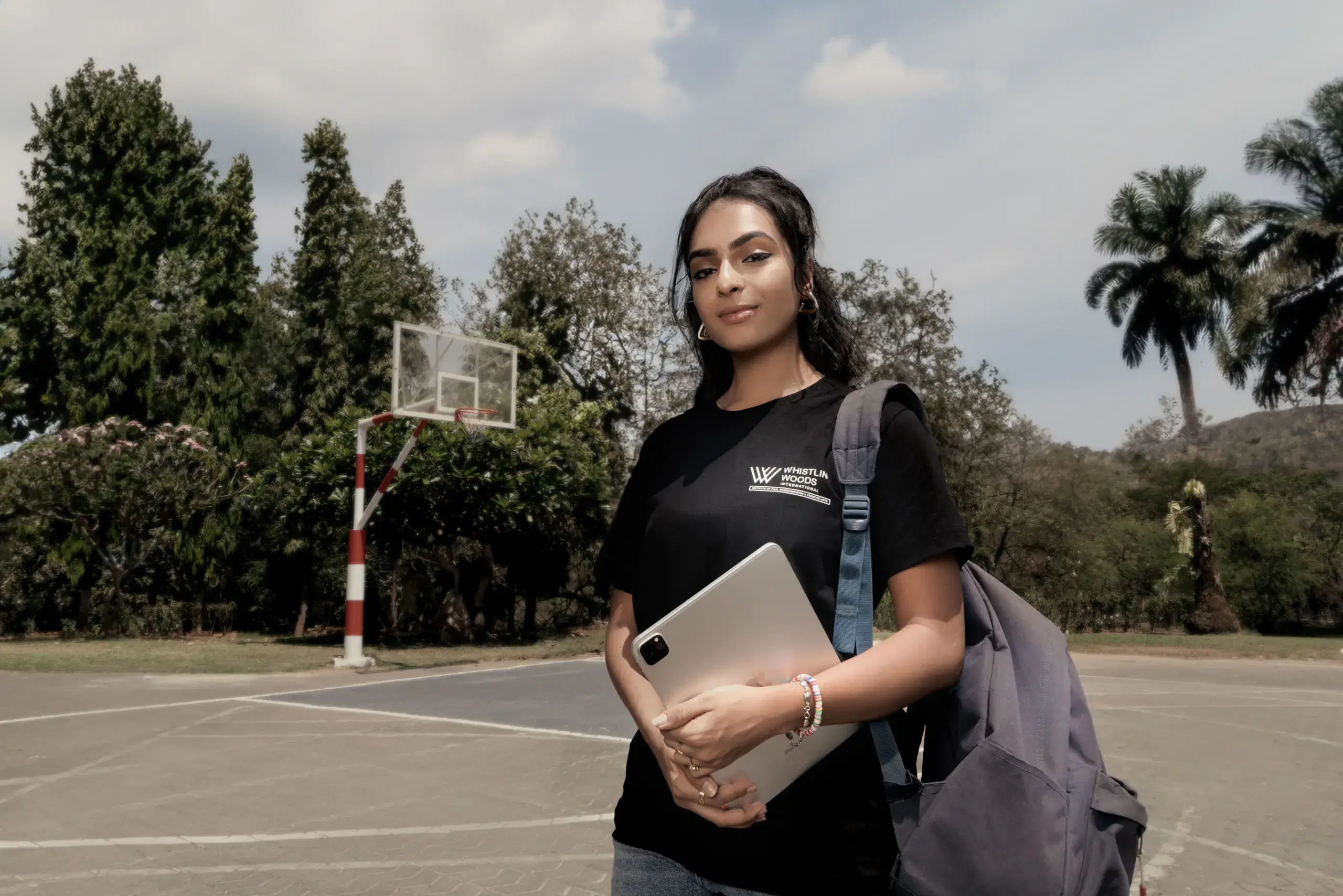 Whistling Woods student with a tablet and backpack on the campus basketball court